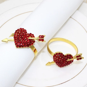Detail of heart-shaped gold napkin rings with red rhinestones on a white linen napkin