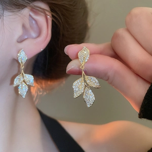 Detailed close-up of leaf-shaped drop earrings with sparkling crystals and gold finish