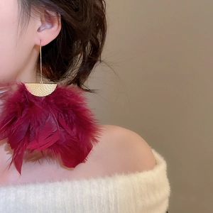 Macro detail of luxury gold circular stud earring with elegant long red feather tassels