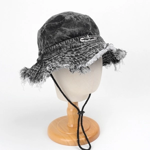 Detail of dark grey washed denim bucket hat with frayed edges and metal pin accessory