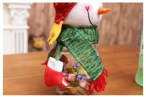 Detail of a snowman-shaped Christmas candy jar with red knit hat and green scarf decor