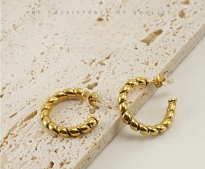 Detail of twisted rope gold C-shape earrings on a textured travertine stone base
