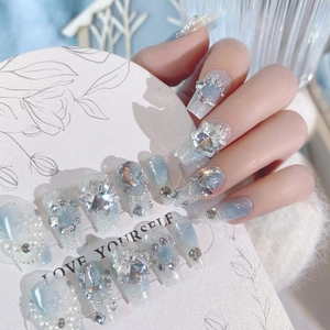 Close-up of blue gradient press-on nails with sparkling rhinestones and snowflake patterns