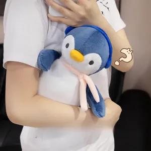 Plush penguin toy with scarf and earmuffs being held to show soft texture and size