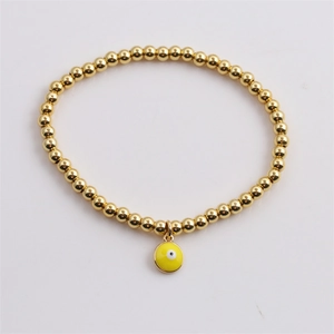 Detail of gold beaded elastic bracelet with yellow evil eye enamel pendant charm