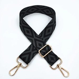 Detail of black and grey geometric diamond pattern woven bag strap with gold metal hooks