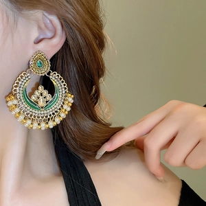 Close-up of ethnic gold drop earrings with green enamel, white pearls, and tassels on model