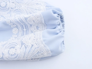 Detailed view of light blue shirt sleeve with white lace embroidery and elastic cuffs