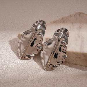 Detailed close-up of metallic irregular folded leaf earrings on a stone platform