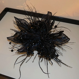 Close-up of black mesh flower hair claw with intricate beadwork and soft feathers