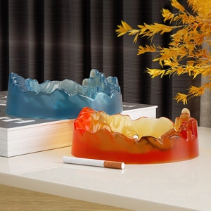 Detail of mountain-shaped resin ashtrays in matte blue and orange on a desk