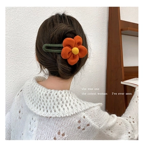 Detail of woman wearing an orange flower hair clip with yellow pistil and green base