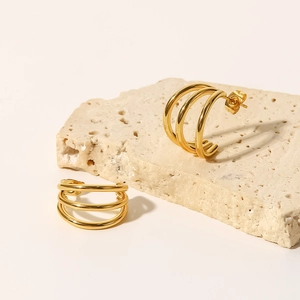 Detailed close-up of 18K gold-plated triple-layered geometric hoop earrings on stone