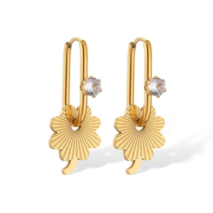 Close-up of gold clover earrings with radial textures and sparkling crystals on white background