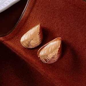 Macro shot of golden shell-textured earrings on a premium dark velvet background