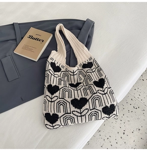 Détail du motif cœur tricoté sur le sac fourre-tout beige posé sur une literie blanche