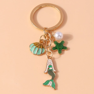 Detail of mermaid, starfish, shell charms and pearl on golden metal keychain ring