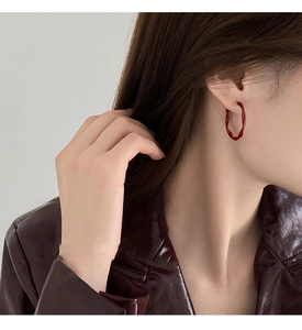 Close-up of red twisted hoop earrings with glossy finish on a model's ear