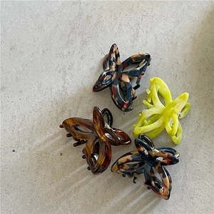 Acetate butterfly hair claws in amber, tortoiseshell and neon green on stone surface