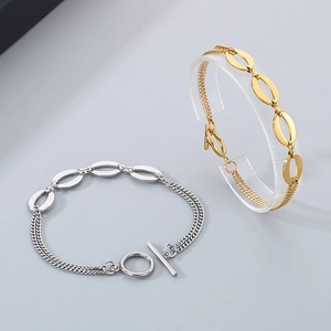 Detail of layered gold and silver chain bracelet featuring toggle clasp on grey surface