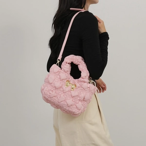 Pink quilted heart shoulder bag with golden chain and bow decoration on a female model