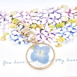 Handmade gold keychain featuring real blue dried flowers inside a round resin pendant