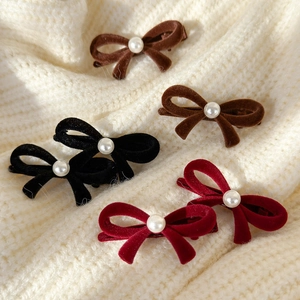 Detailed view of six velvet bow hair clips with pearls on a soft knit sweater background