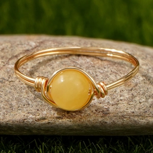 Detail van een handgemaakte goudkleurige ring met gele edelsteen op een natuursteen