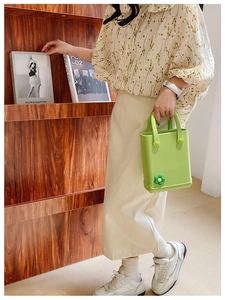 Detail der hellgrünen EVA-Tasche mit 3D-Blumen-Accessoires, gehalten von einem Model in Bluse