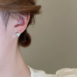 Close-up of a silver heart-shaped stud earring with white inlay on a model's ear