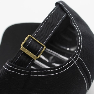 Detail of black cotton baseball cap rear strap with contrast stitching and gold buckle