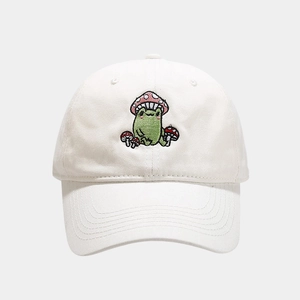 Close-up of cute green frog and red mushroom embroidery on a cream cotton baseball cap