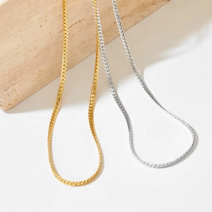 Detail of gold and silver stainless steel flat snake chain necklaces on beige stone