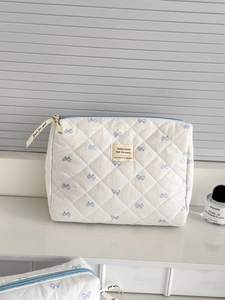 Detail of white quilted makeup bag with blue bows and Just for you ribbon zipper pull