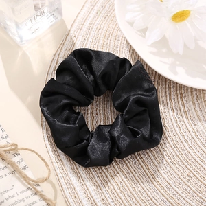 Classic black satin scrunchie with soft pleats on a minimalist woven mat background