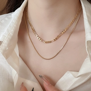 Close-up of 18k gold plated layered necklace featuring figaro and snake chains on a model