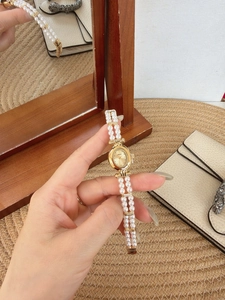 Detailed shot of retro oval gold watch with double-strand pearl bracelet and shell dial