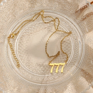 Close-up of golden number 777 pendant on stainless steel necklace over textured fabric