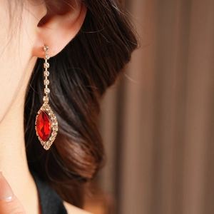 Close-up of elegant gold drop earrings with a red crystal and sparkling rhinestones
