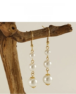 Detailed view of long gold drop earrings with white pearls hanging on a wooden stand