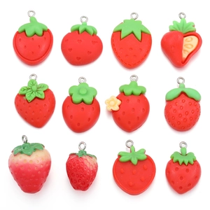 Detail view of various red resin strawberry pendants with green leaves for DIY jewelry crafts