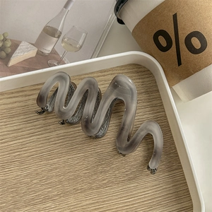 Detailed view of gray wavy acetate claw clip with marble texture on wooden tray