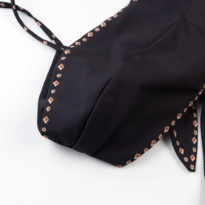 Detail view of black swimwear fabric with geometric orange diamond pattern and fine stitching