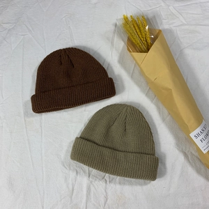 Detailed knit texture of brown and olive green beanie hats on a textured white fabric