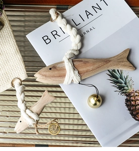 Detail view of wooden fish pendants with rustic hemp rope and metallic bell accents