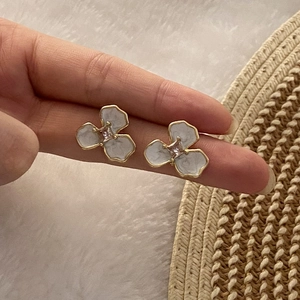 Three-petal flower stud earrings with gold edges and pink zircon center held by hand