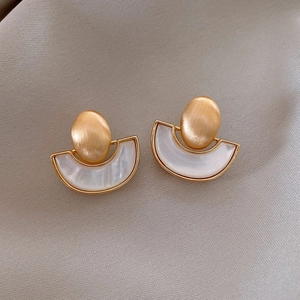 Detailed close-up of golden geometric earrings with white resin inlay on grey fabric