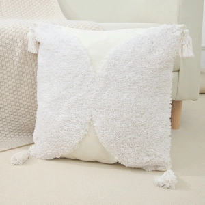 Close-up of bohemian white tufted pillow cover with fringe tassels on a beige sofa