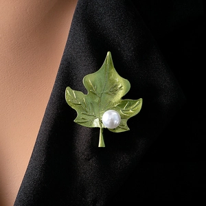 Detailed close-up of a green leaf brooch with a white pearl on a black suit lapel