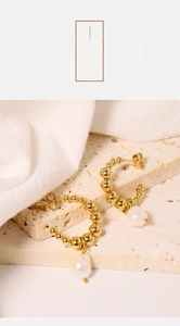 Detail of gold beaded C-shaped earrings with baroque pearls on a textured stone surface